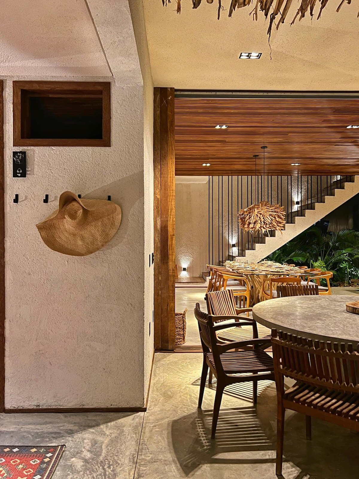 Chapéu de palha pendurado na parede do hall, com a sala de jantar e a escada ao fundo