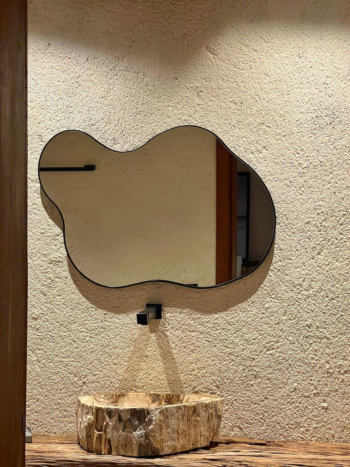 Espelho de formato orgânico sobre cuba de pedra, em parede de textura clara