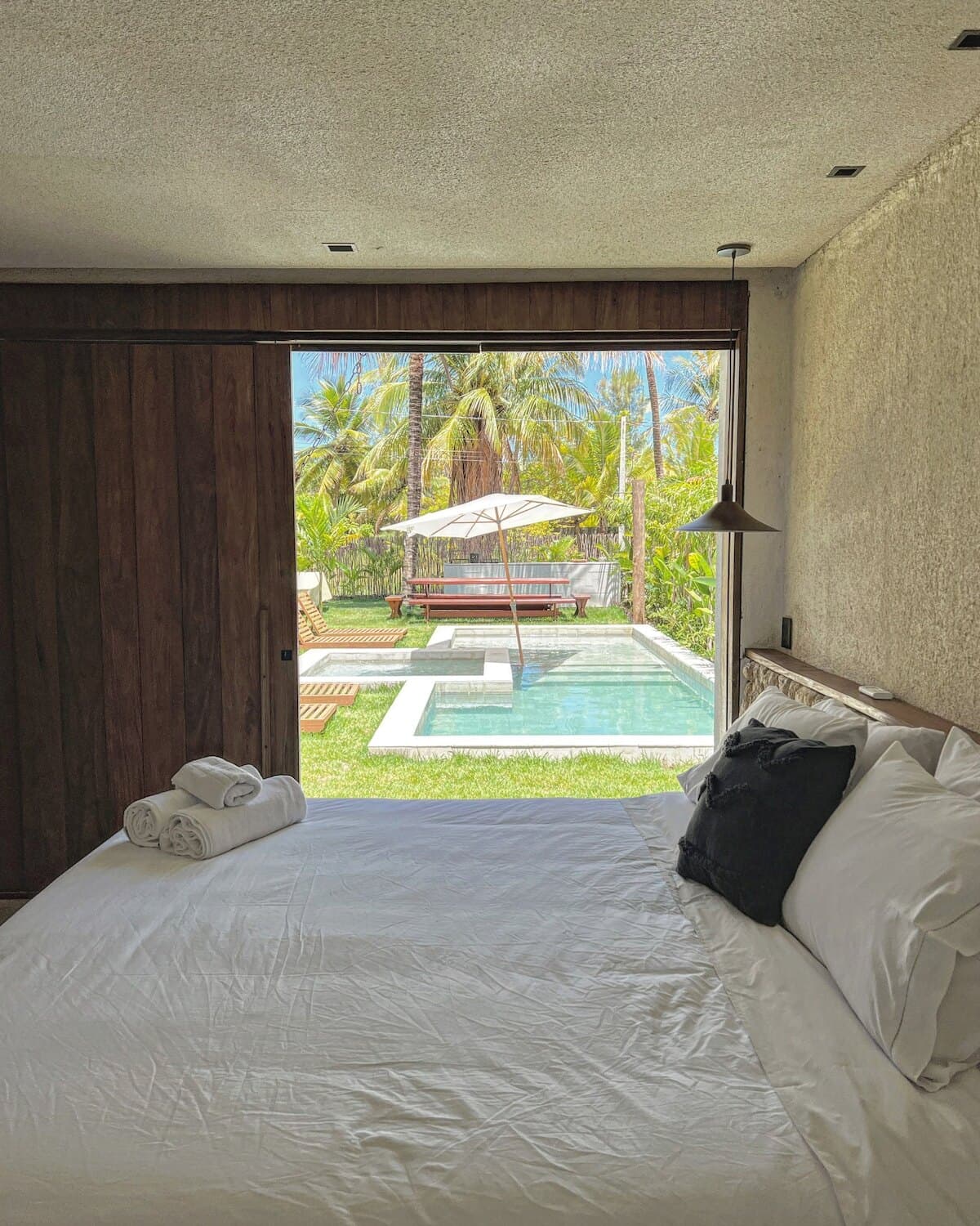 Quarto com a cama voltada para a porta aberta, que enquadra a piscina e a jacuzzi do jardim