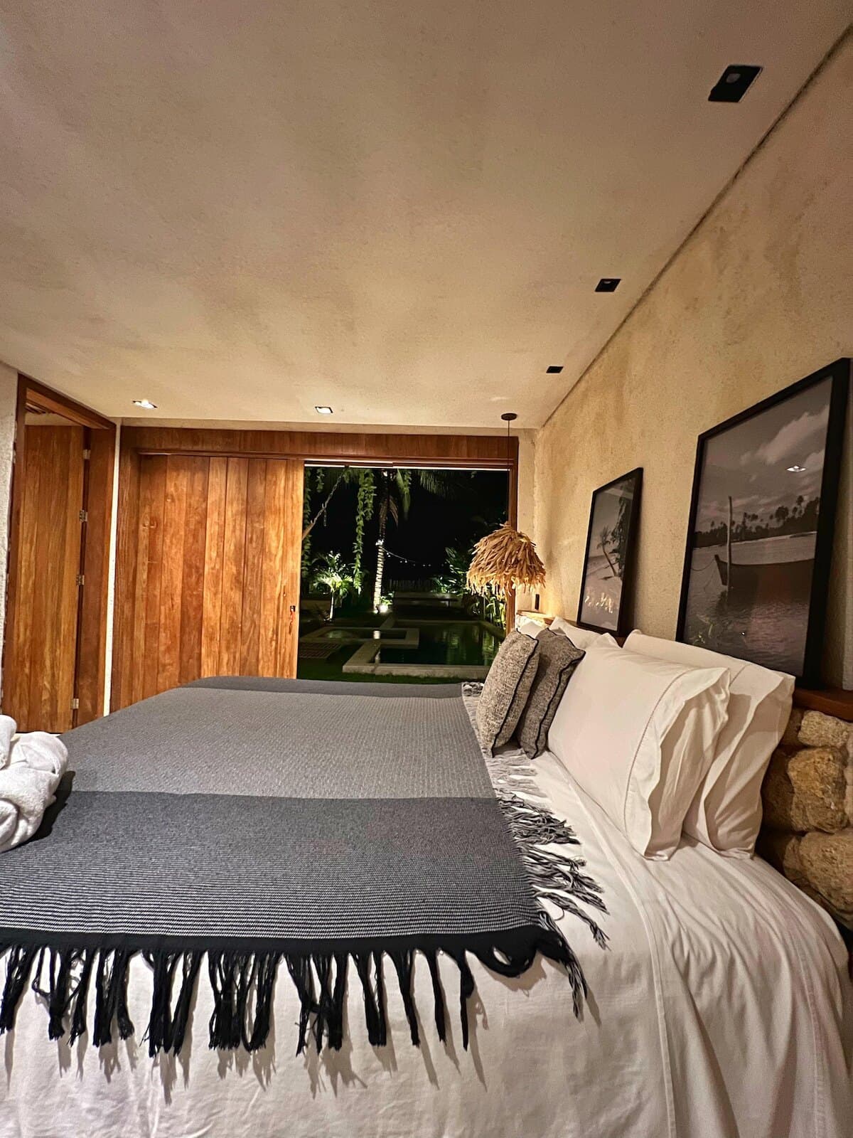 Cama com manta cinza e preta e, ao fundo, a porta de madeira que dá para o jardim